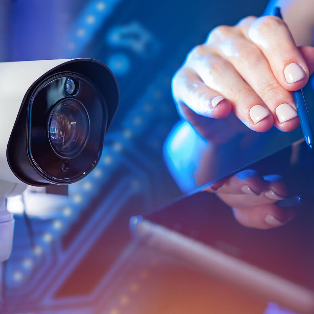 CCTV system application concept. CCTV camera next to woman's hands. Smartphone in hands of businesswoman close up. Remote video surveillance metaphor. Remote monitoring of video surveillance system